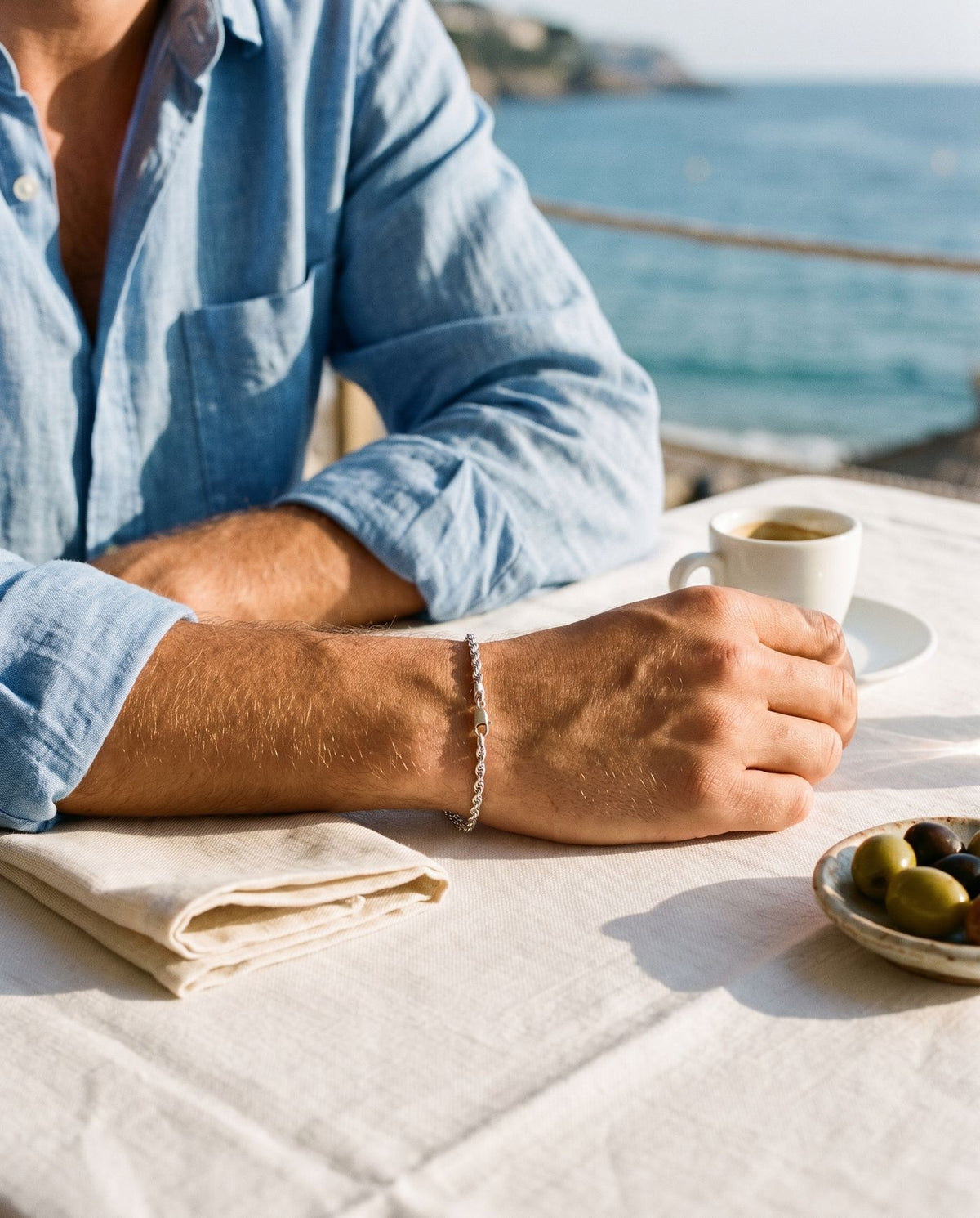 Fine rope chain bracelet on a wrist at a seaside cafe table