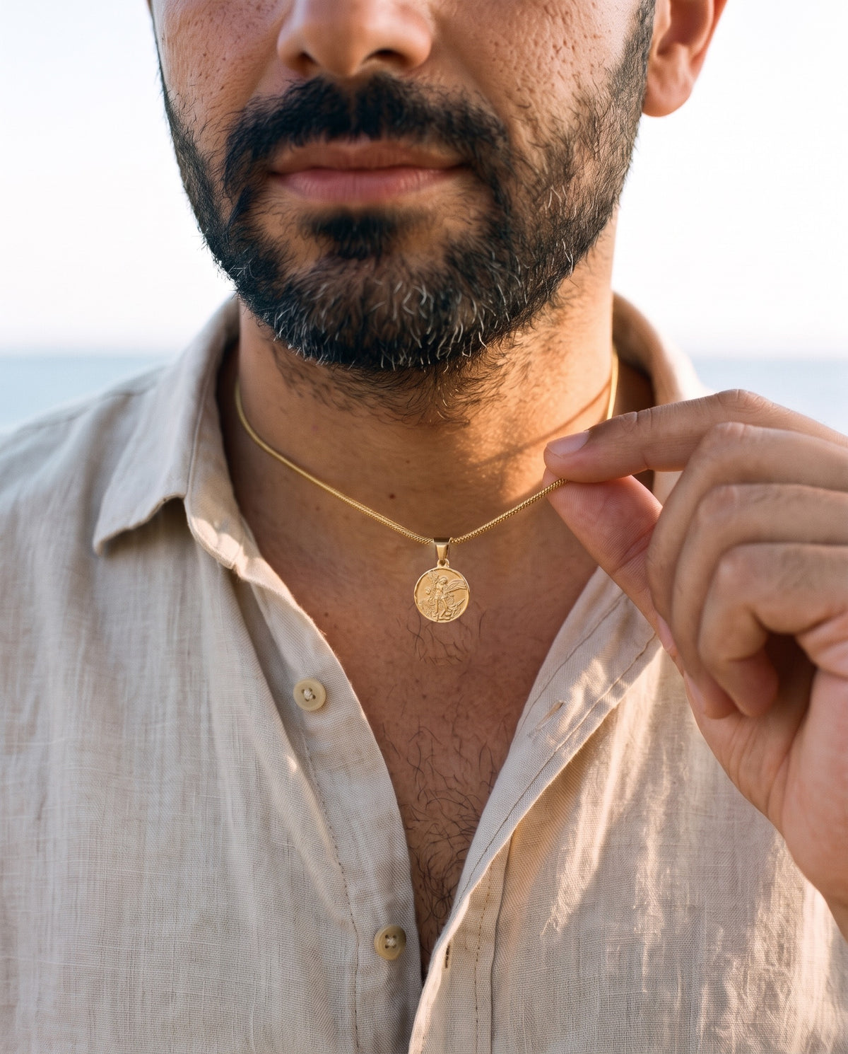 Man adjusting the Marco Maveri Archangel Medallion Snake Chain Necklace, close-up, Gold