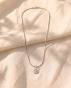 Marco Maveri Archangel Medallion Snake Chain Necklace laid on cream linen, Silver