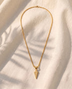 Marco Maveri Arrowhead Pendant Wheat Chain Necklace laid on cream linen, Gold