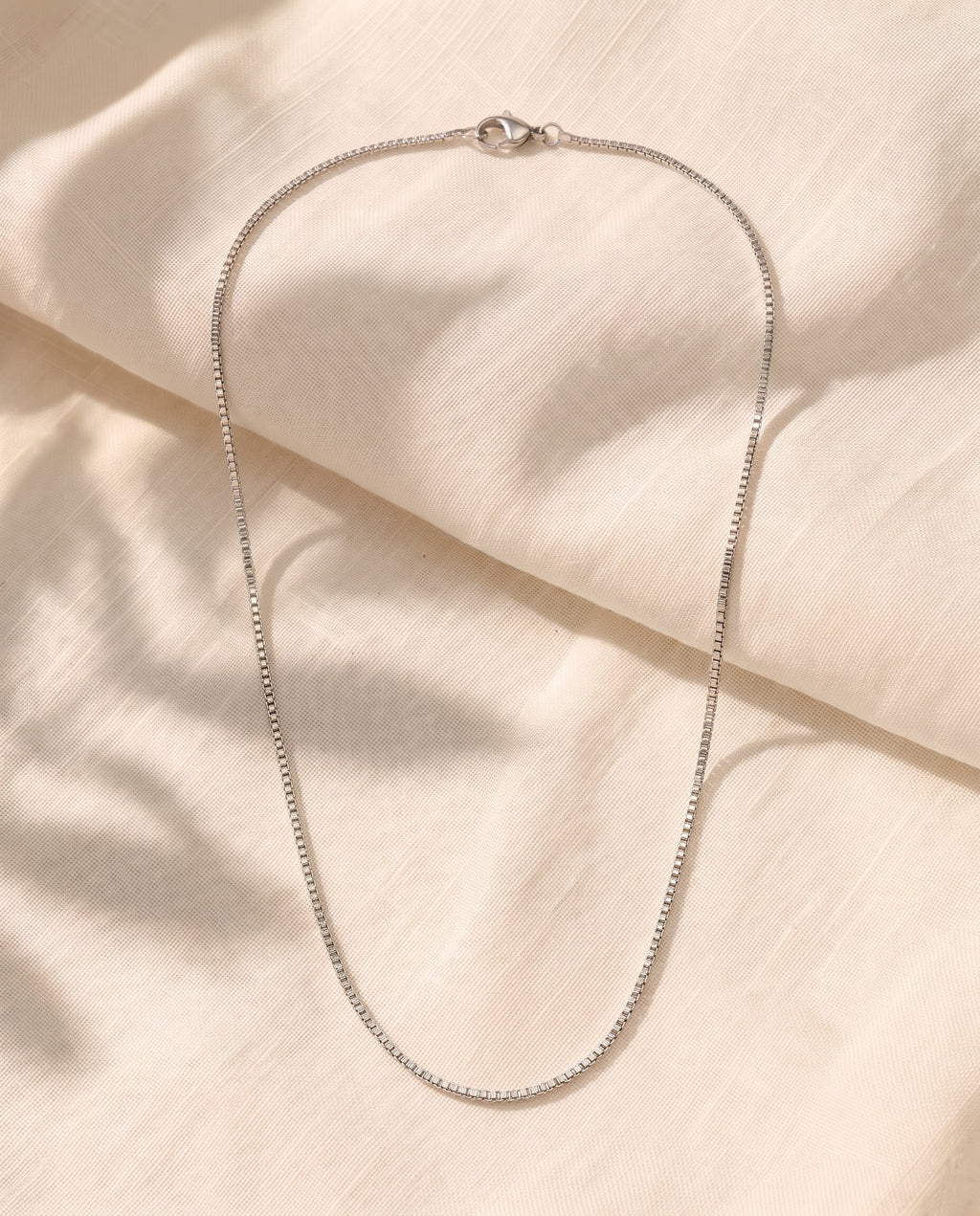 Marco Maveri Box Chain Necklace in Titanium Steel laid on cream linen, Silver