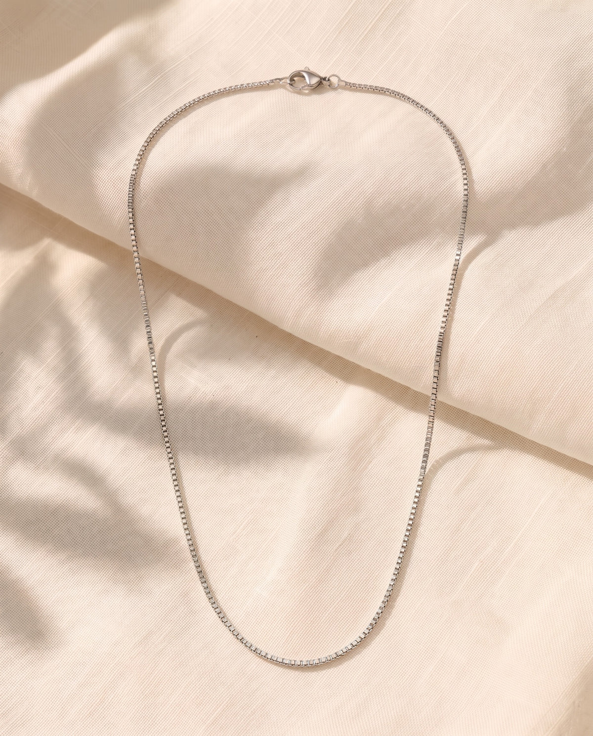 Marco Maveri Box Chain Necklace in Titanium Steel laid on cream linen, Silver