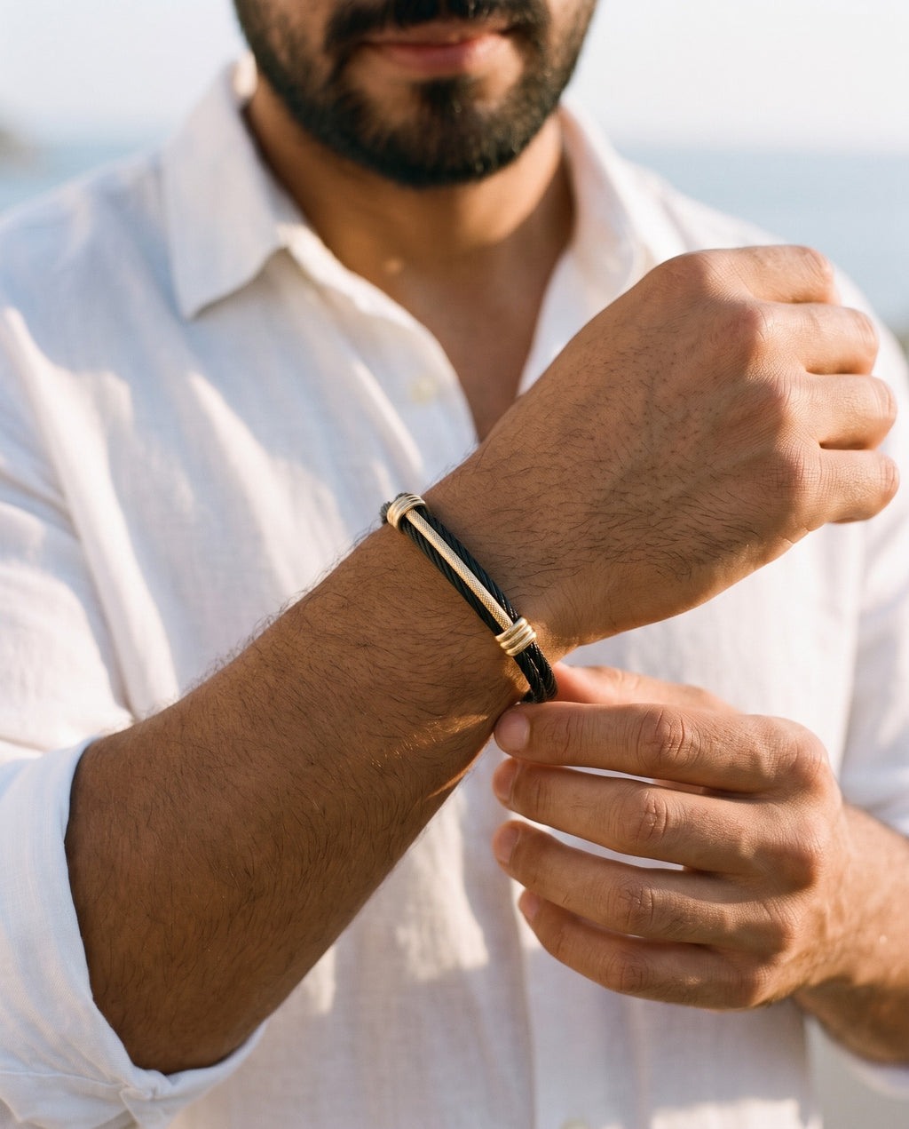 Man adjusting the Marco Maveri Cable Cuff Bracelet, close-up, Black / Gold