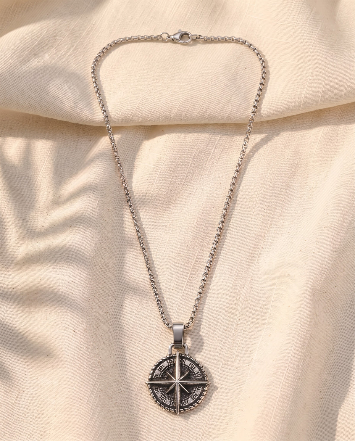 Marco Maveri Compass Pendant Necklace laid on cream linen, Silver