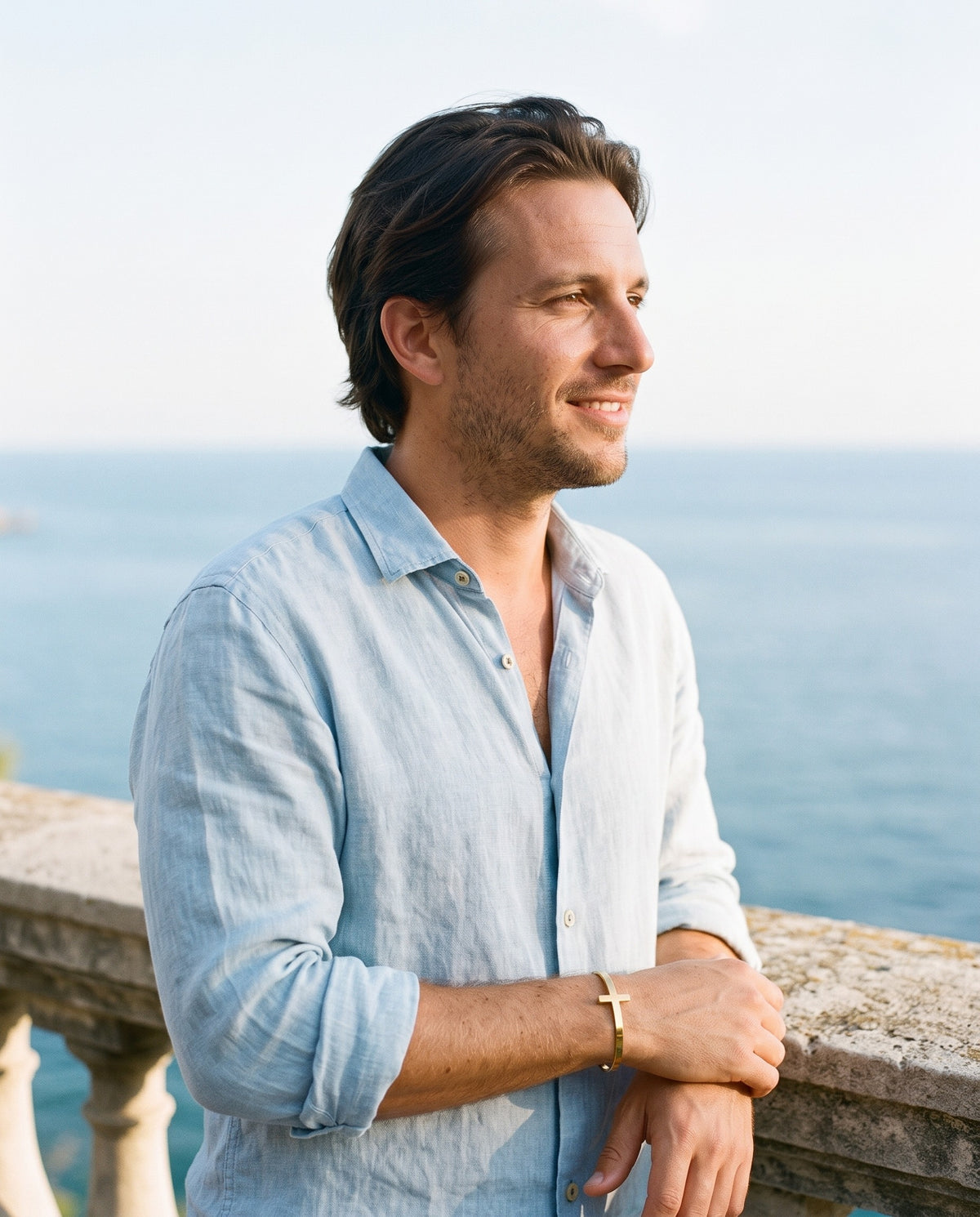 Man wearing the Marco Maveri Cross Motif Cuff Bracelet by the sea, Gold