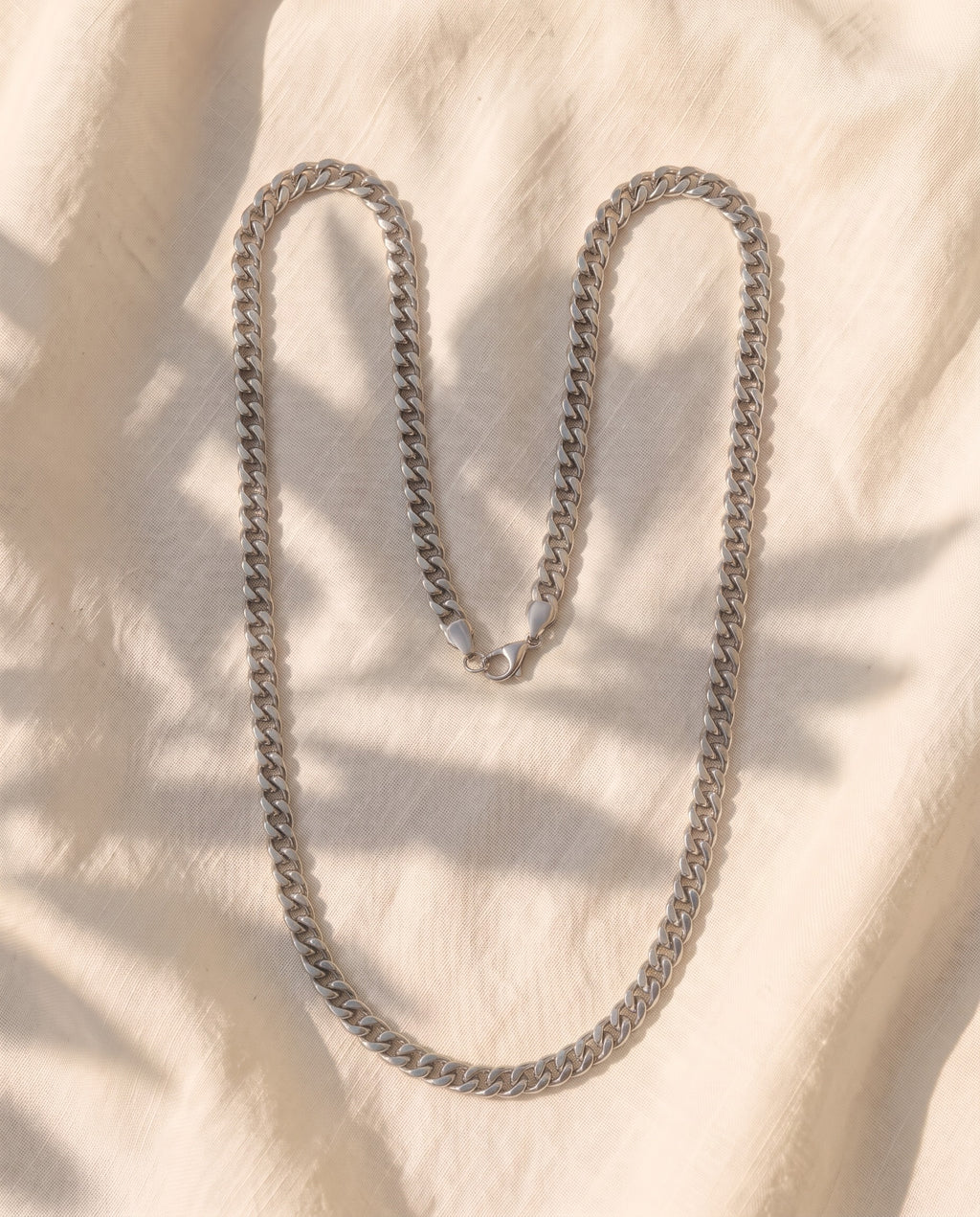 Marco Maveri Cuban Link Chain Necklace laid on cream linen, Silver