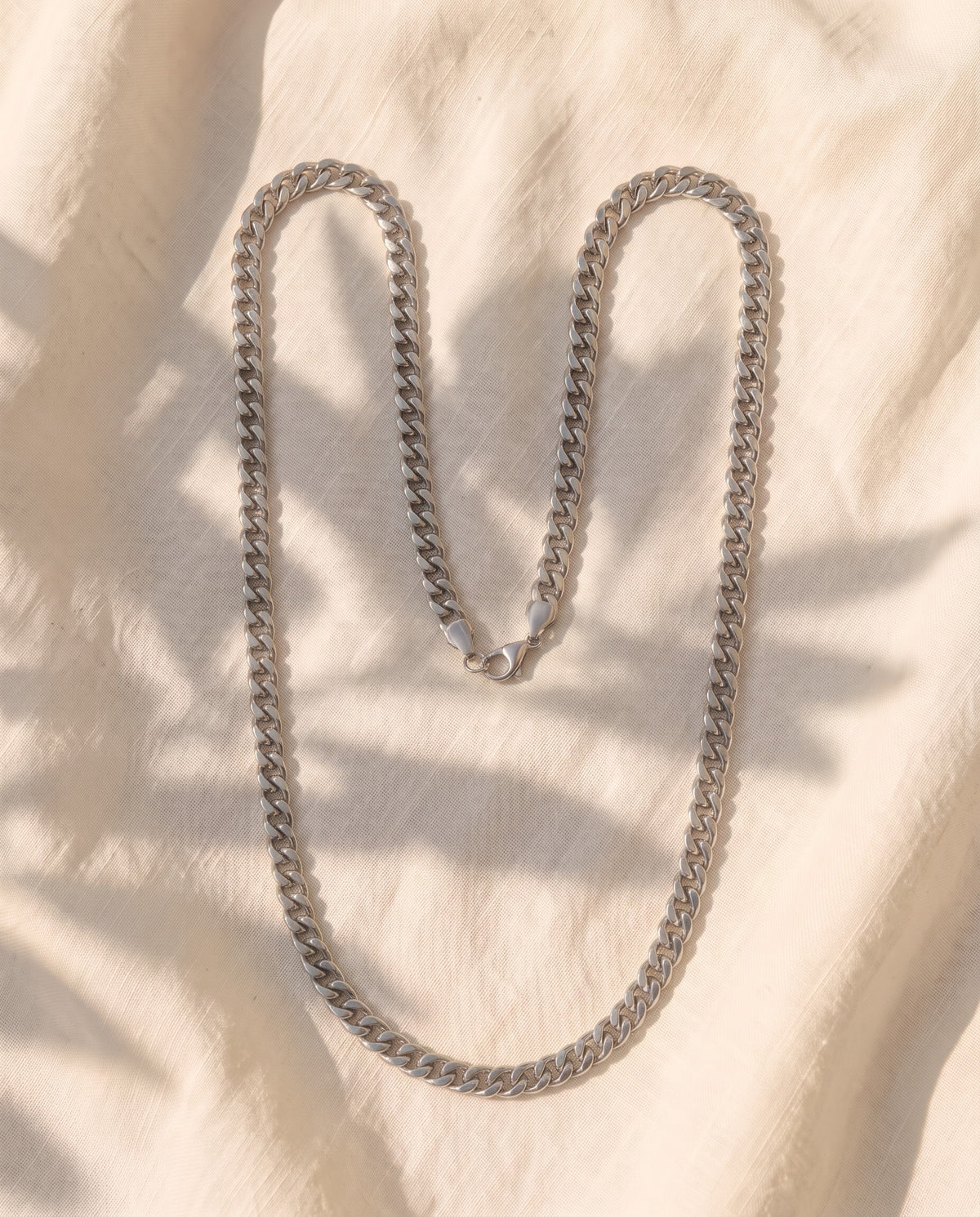 Marco Maveri Cuban Link Chain Necklace laid on cream linen, Silver