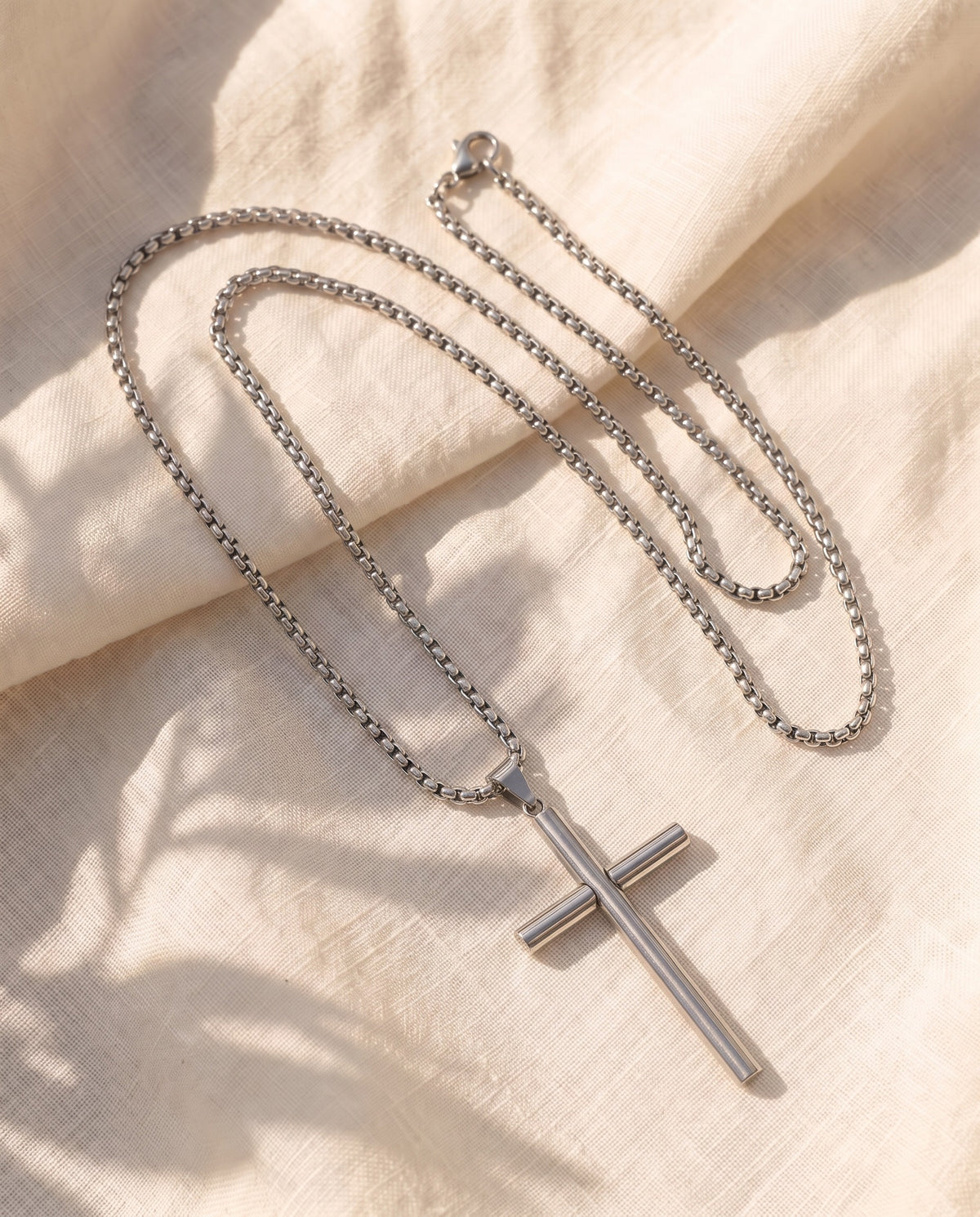Marco Maveri Cylindrical Cross Pendant Necklace laid on cream linen, Silver