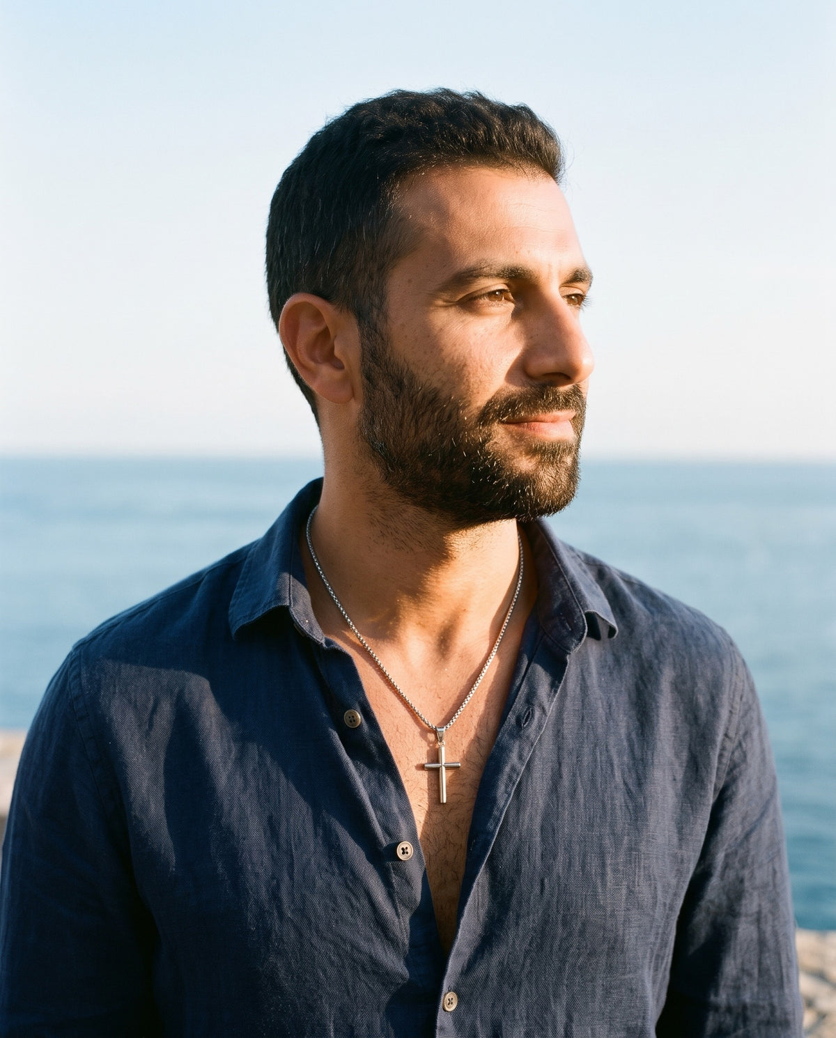 Man wearing the Marco Maveri Cylindrical Cross Pendant Necklace by the sea, Silver