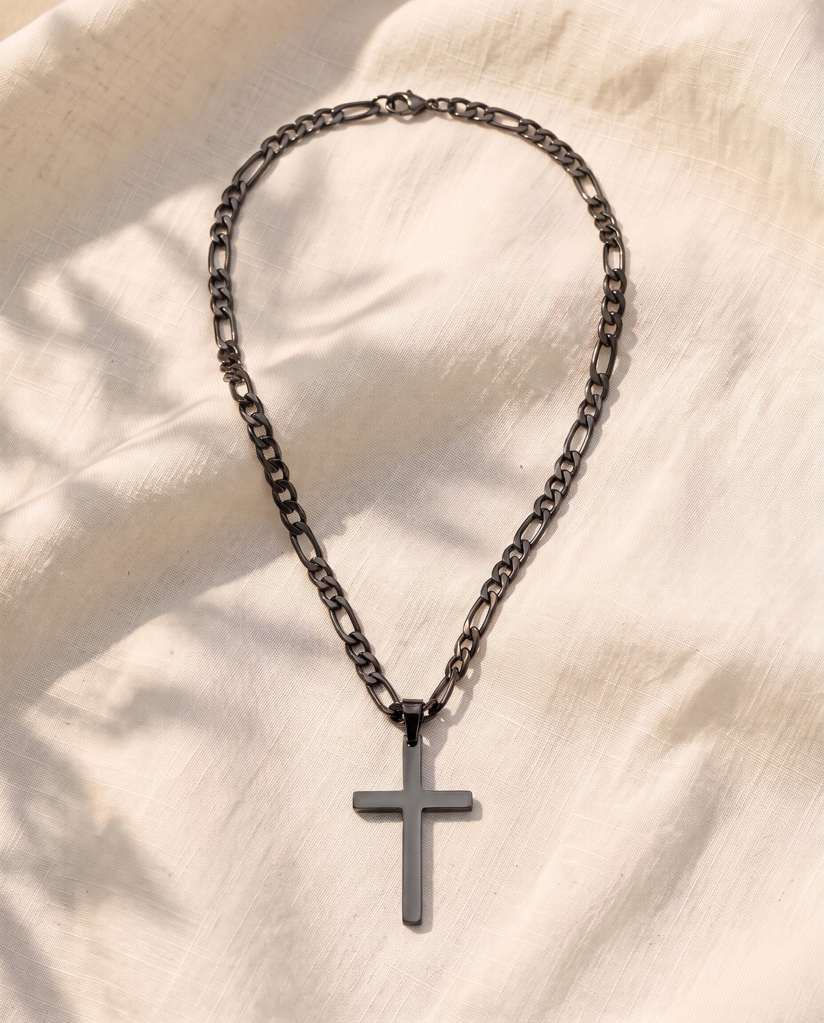 Marco Maveri Figaro Chain with Cross Pendant laid on cream linen, Black