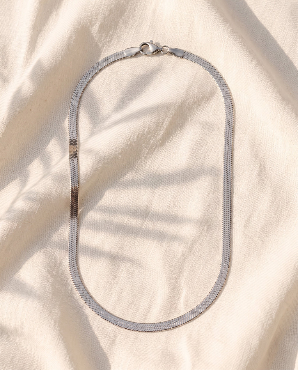 Marco Maveri Flat Snake Chain Necklace laid on cream linen, Silver