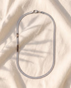 Marco Maveri Flat Snake Chain Necklace laid on cream linen, Silver
