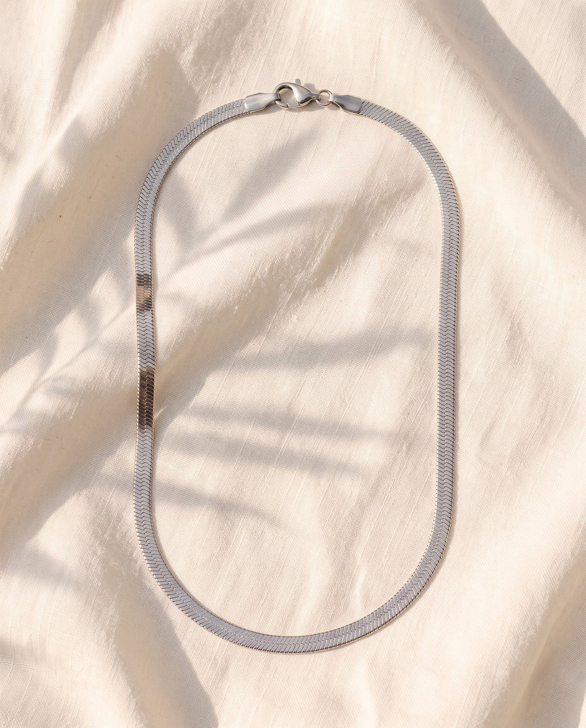 Marco Maveri Flat Snake Chain Necklace laid on cream linen, Silver