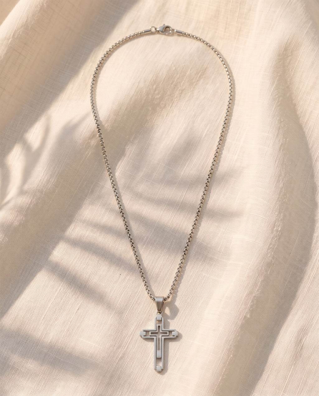 Marco Maveri Hollow Double Cross Pendant Necklace laid on cream linen, Silver