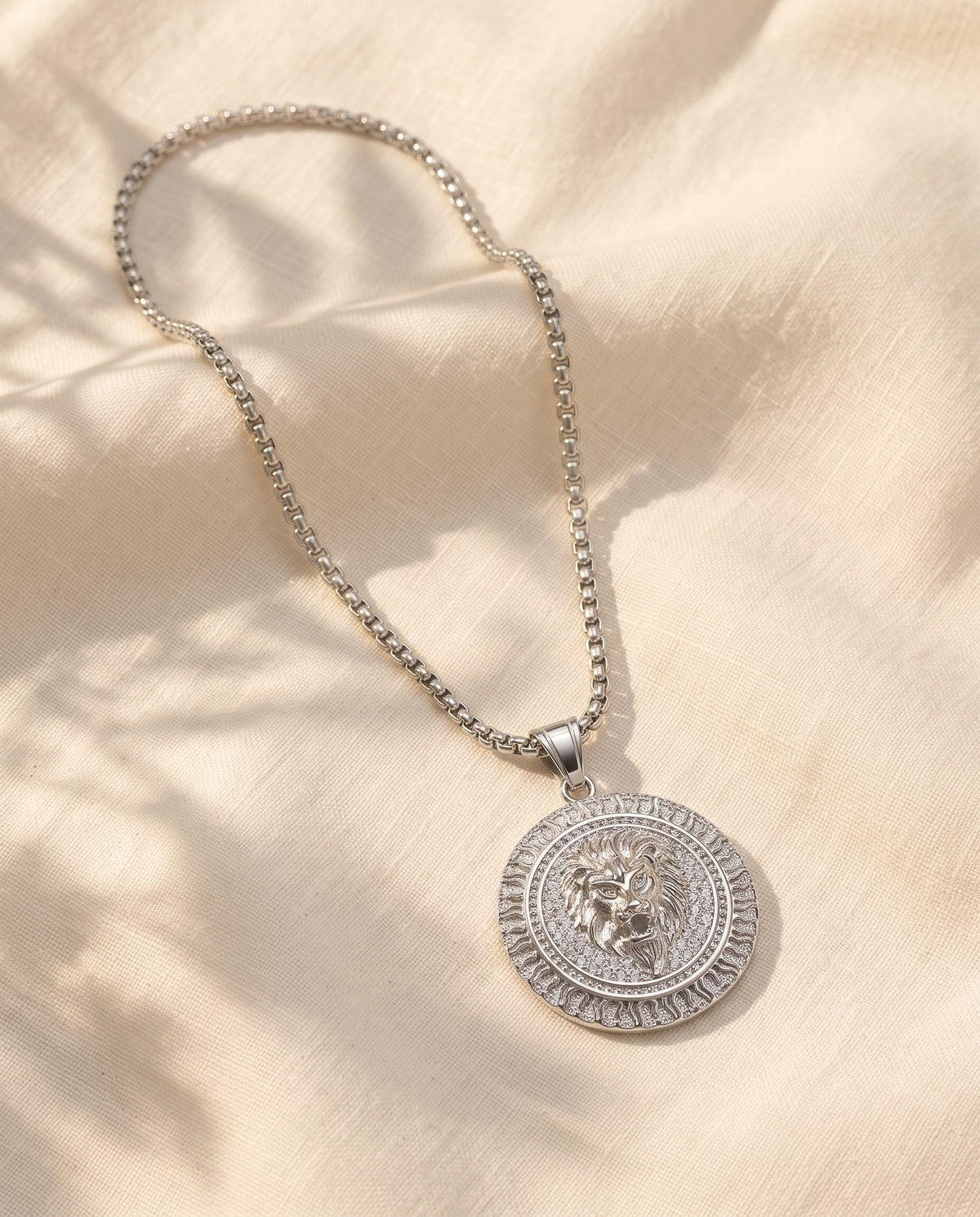 Marco Maveri Lion Head Medallion Pendant Necklace laid on cream linen, Silver