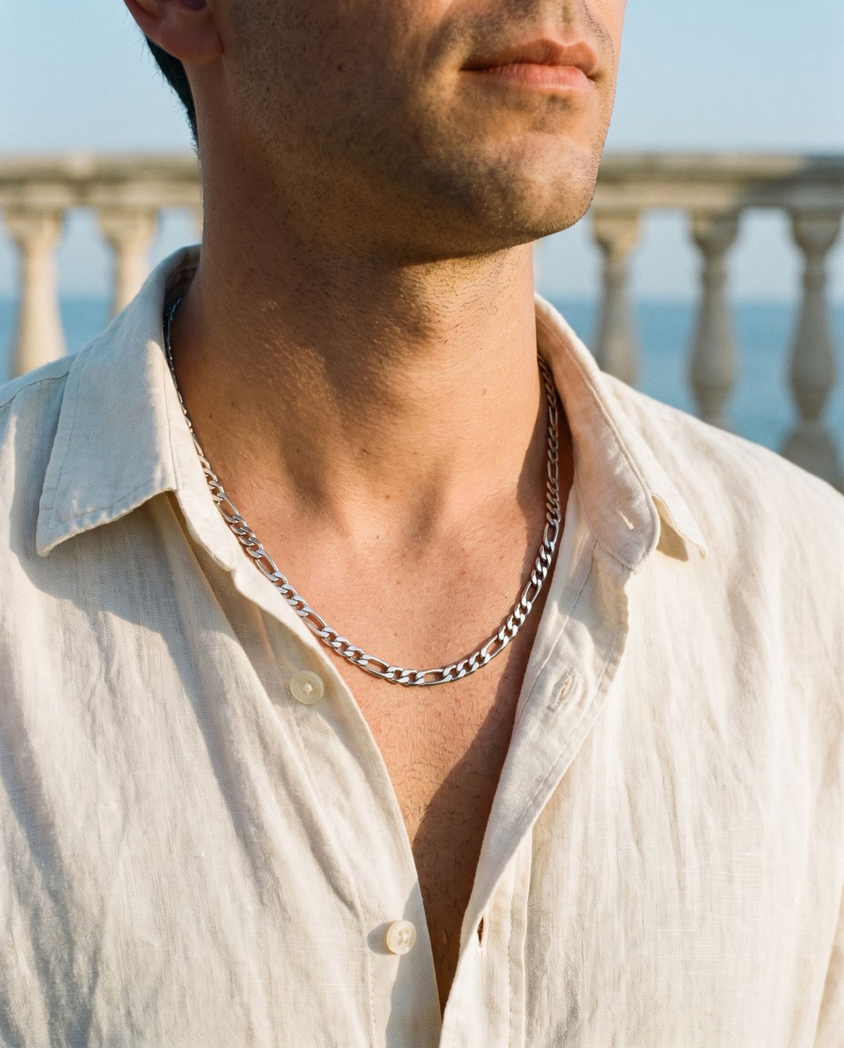Figaro chain resting on the collarbone under an open linen shirt