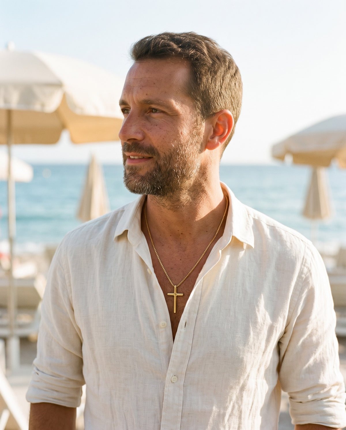 Man wearing the Marco Maveri Minimalist Cross Pendant Necklace by the sea, Gold