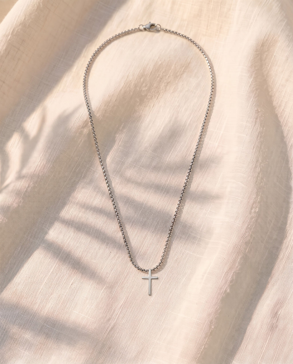 Marco Maveri Minimalist Cross Pendant Necklace laid on cream linen, Silver