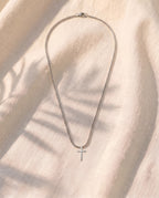 Marco Maveri Minimalist Cross Pendant Necklace laid on cream linen, Silver
