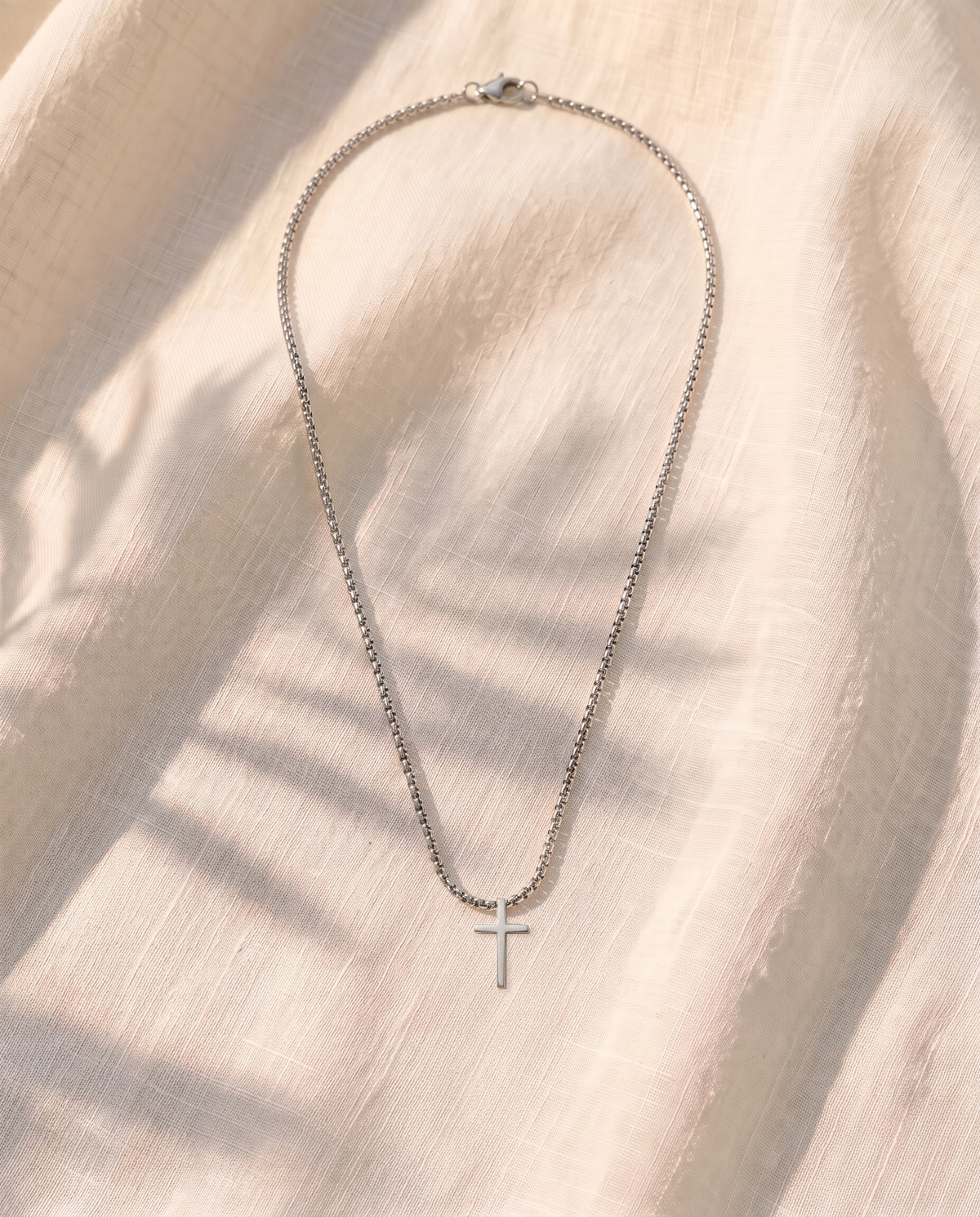 Marco Maveri Minimalist Cross Pendant Necklace laid on cream linen, Silver