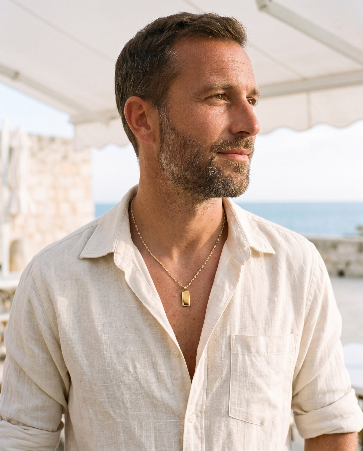 Man wearing the Marco Maveri Rectangular Bar Pendant Necklace by the sea, Gold