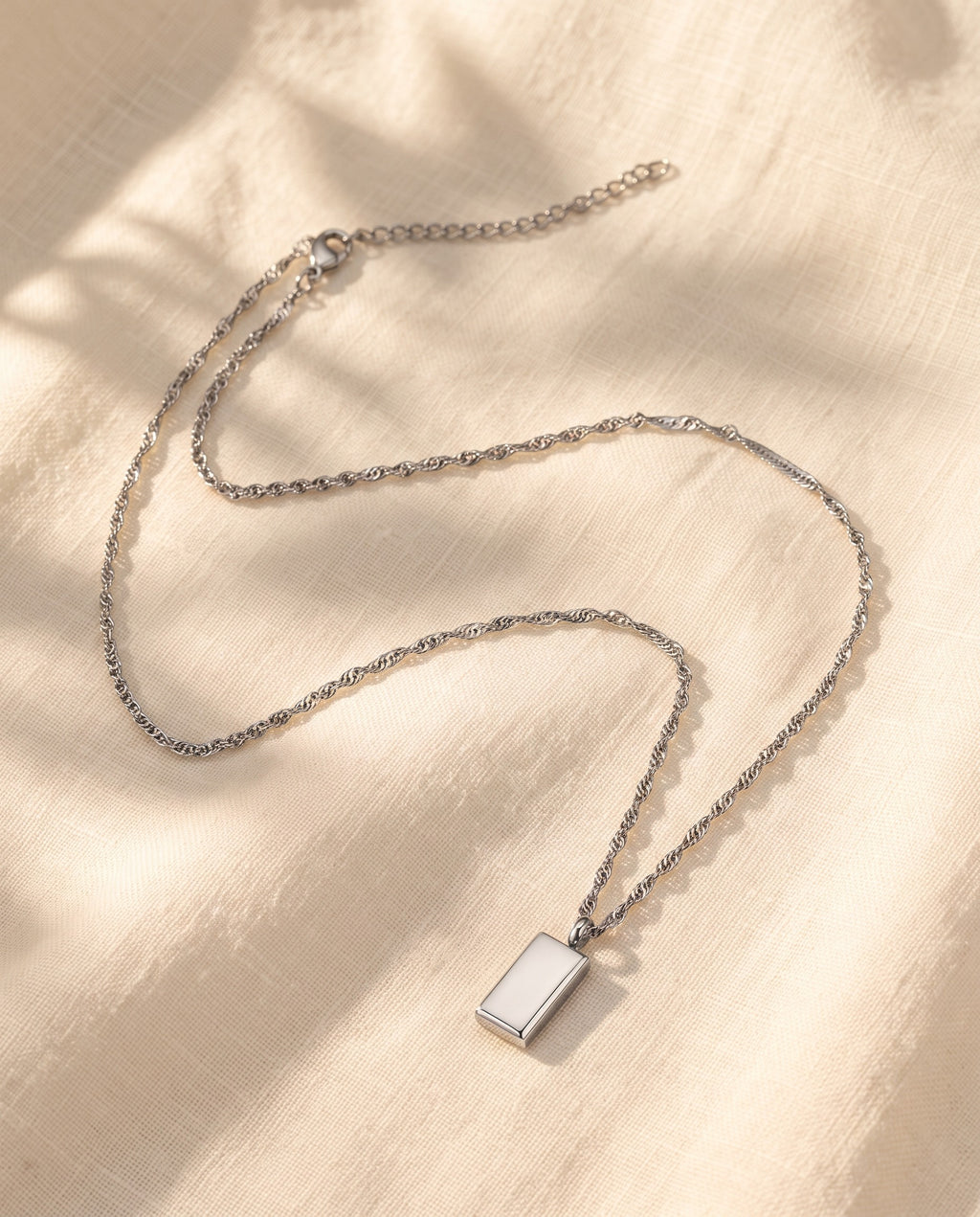 Marco Maveri Rectangular Bar Pendant Necklace laid on cream linen, Silver