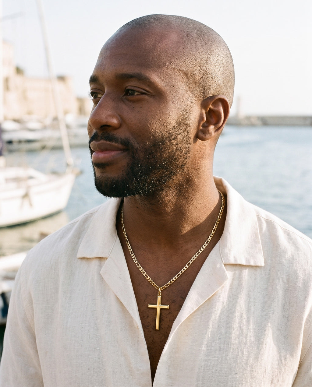 Man wearing the Marco Maveri Slim Cross Pendant Necklace by the sea, Gold