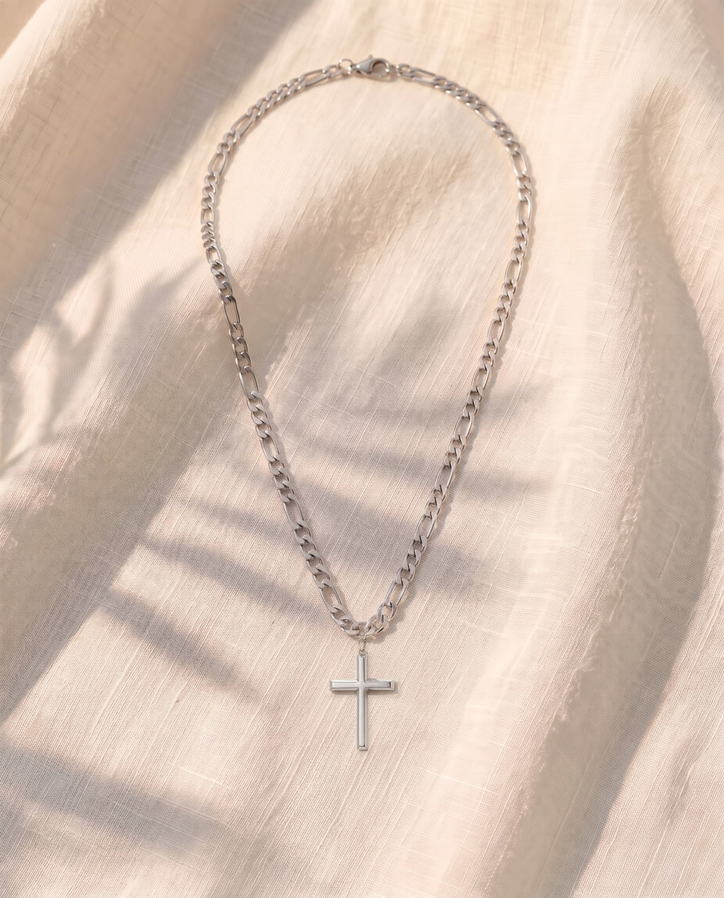 Marco Maveri Slim Cross Pendant Necklace laid on cream linen, Silver