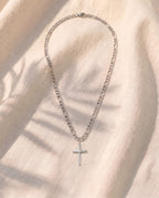 Marco Maveri Slim Cross Pendant Necklace laid on cream linen, Silver