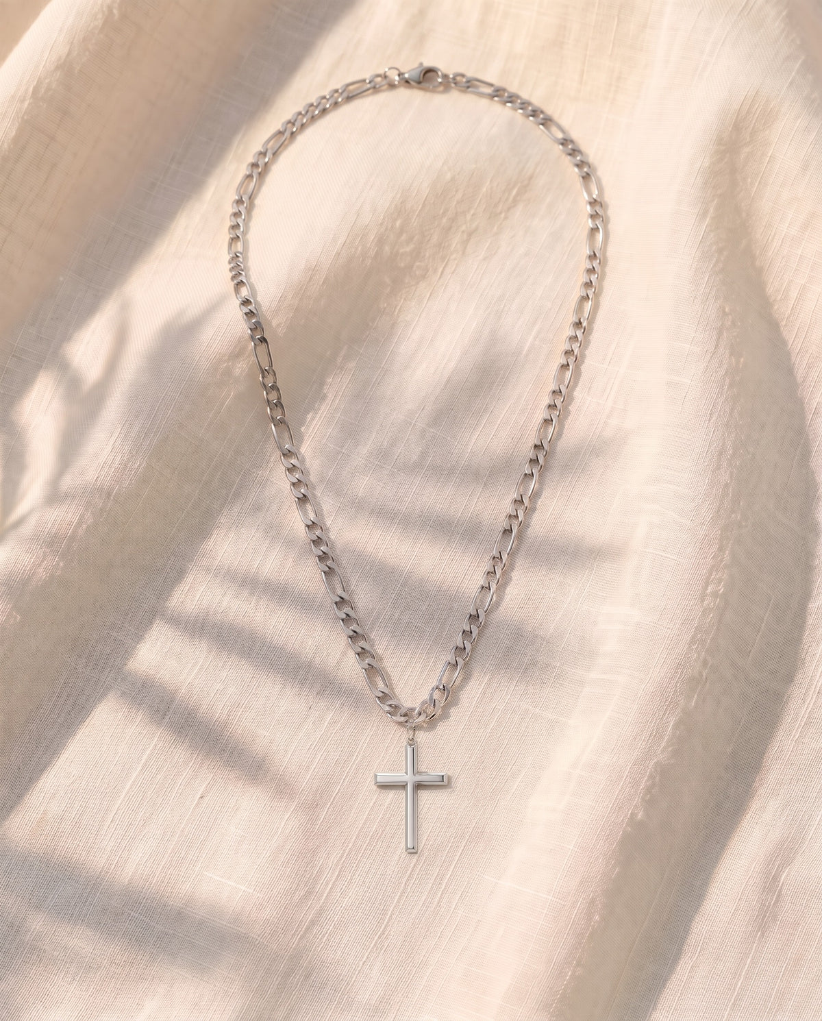 Marco Maveri Slim Cross Pendant Necklace laid on cream linen, Silver
