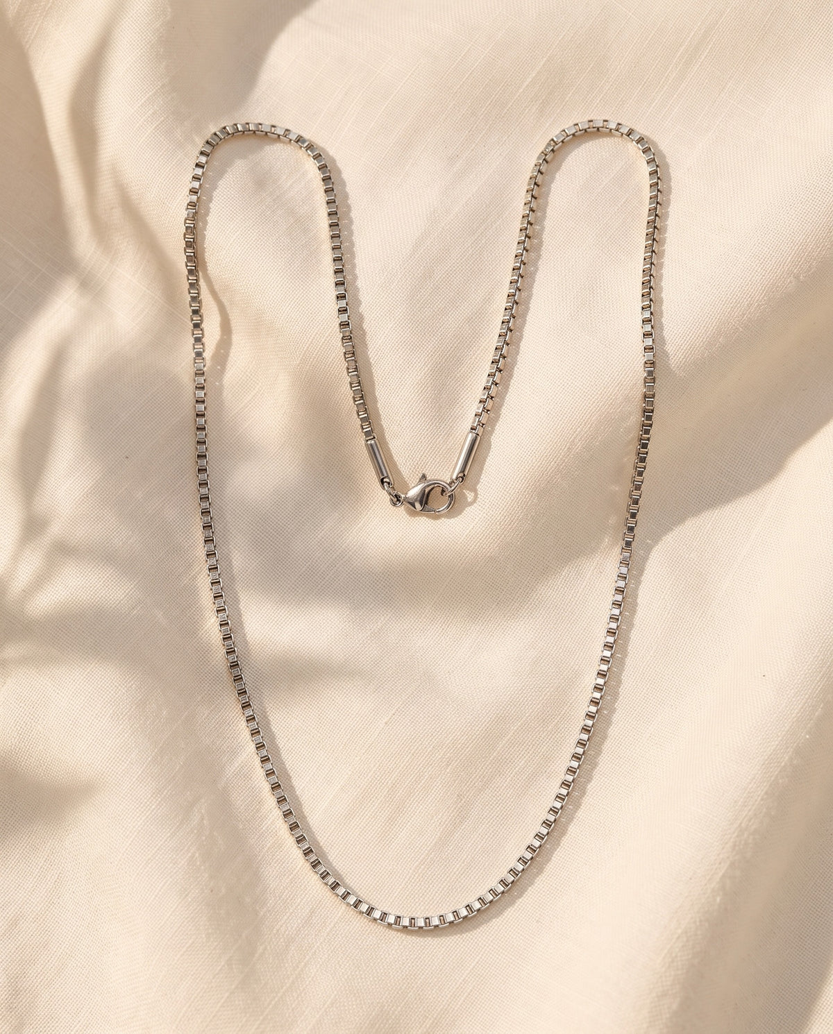 Marco Maveri Stainless Steel Box Chain Necklace laid on cream linen, Silver