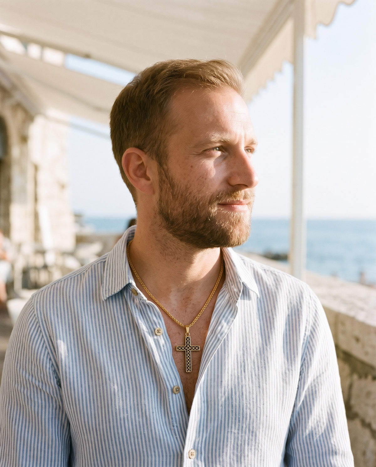 Man wearing the Marco Maveri Textured Cross Pendant Necklace by the sea, Gold