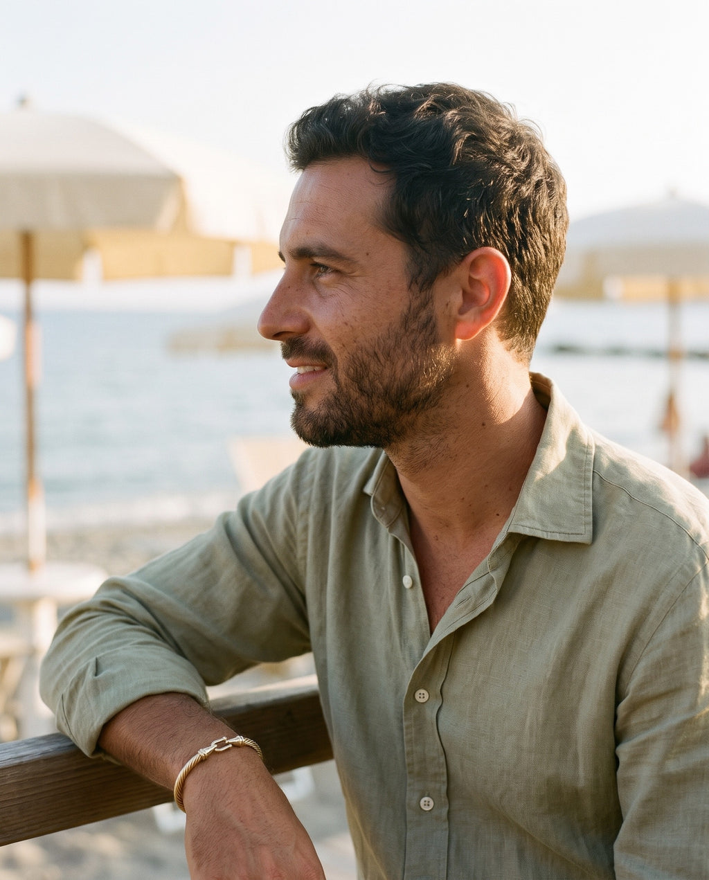 Man wearing the Marco Maveri Twisted Steel Hook Bangle by the sea, Gold