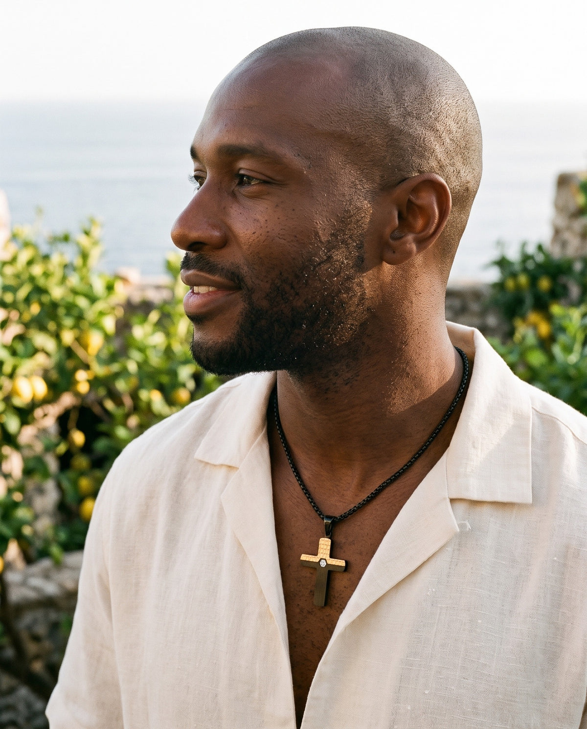 Man wearing the Marco Maveri Two-Tone Inlaid Cross Pendant Necklace by the sea, Black / Gold