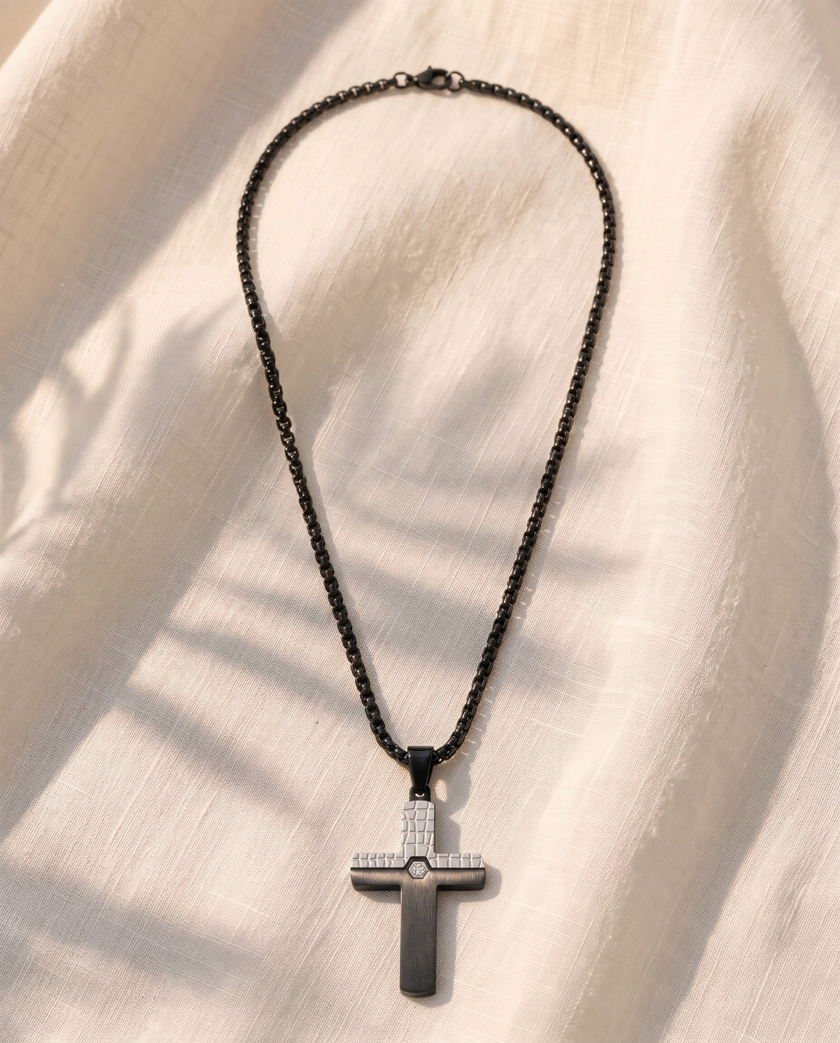 Marco Maveri Two-Tone Inlaid Cross Pendant Necklace laid on cream linen, Black / Silver